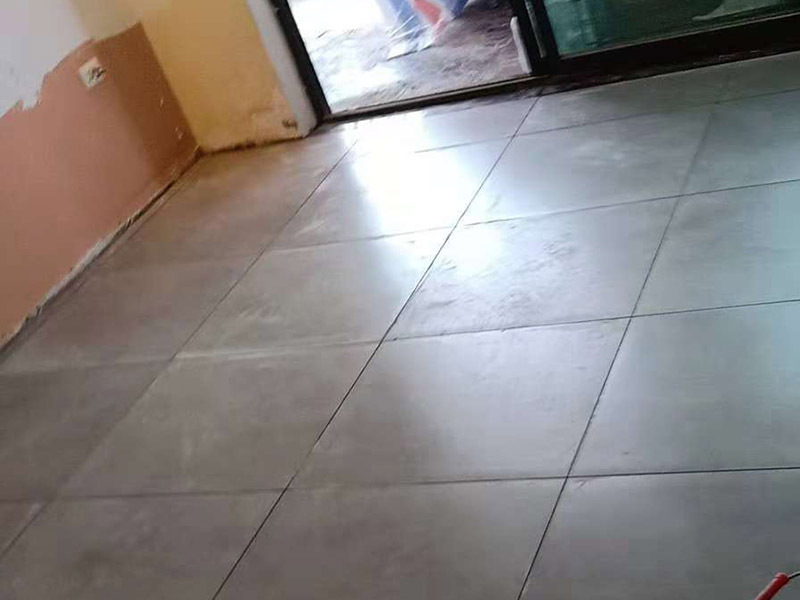 客廳地磚鋪貼：鋪貼的工具包括橡膠錘和粘結(jié)劑。在進(jìn)行施工之前先把所需要的這些材料都整理好放在一旁備用；基層的處理工作對(duì)瓷磚的平整度有很大的影響，對(duì)于基層要做好清潔工作，還有找平工作。放樣：在進(jìn)行瓷磚的鋪貼工作之前還事先找好垂直線，這樣可以在鋪貼的時(shí)候找到瓷磚的水平線，讓瓷磚鋪貼的更加的平整。粘結(jié)劑加水?dāng)嚢杈鶆?，靜置10分鐘之后就可以使用。將瓷磚表面的浮灰清除，再在瓷磚背面均勻的涂抹上粘結(jié)劑，按照預(yù)鋪的順序?qū)⒋纱u鋪貼在地面上，最后用橡膠錘輕輕拍打至服帖齊整。