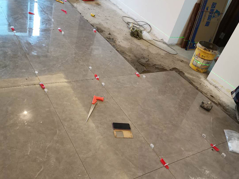 客廳地磚鋪貼：地磚鋪貼前，應(yīng)將地面清掃干凈，尤其是凝結(jié)后的混凝土，否則，地磚鋪貼后會(huì)出現(xiàn)翹邊、空鼓等現(xiàn)象，然后再灑水潤濕地面。地面充分濕潤，但不能有積水，然后將3:1混合好的沙子水泥鋪在地面上，進(jìn)行基層處理。在地磚背面均勻抹水泥砂漿作為粘合層，厚度不低于1cm，然后鋪在剛才試鋪的位置上，用橡皮錘輕敲地磚飾面直至密實(shí)平整達(dá)到要求。地磚鋪完后24h進(jìn)行清理勾縫，勾縫前應(yīng)先將地磚縫隙內(nèi)雜質(zhì)擦凈，用專用填縫劑勾縫，完工后（一般宜在24h之后）再用棉紗等物對(duì)地磚表面進(jìn)行清理。