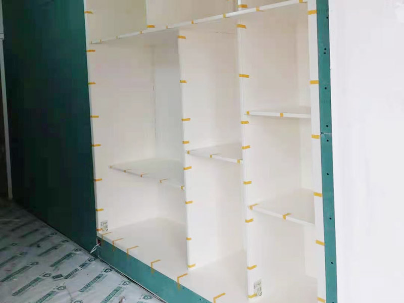 客廳定制柜體安裝：用墊布點(diǎn)好地板，先從靠墻的一端寬側(cè)板開始組裝，將寬側(cè)板平放于地面上（離后墻面保持700mm間隔）。首先將填好的三合一膠塞的板件，平放在墊布上，檢查孔距與圖紙相符，并裝上三合一單連桿。然后將固層釘上木塞，固定于寬側(cè)板上面，頂板大柄孔朝上，其余固層都朝下，腳線大柄孔朝內(nèi)（中間固層與L架高度一致，即底板到固層內(nèi)空為960mm，現(xiàn)場打?qū)影蹇祝７派蟼?cè)板，釘上木塞，木塞要求連通兩邊的固層。在第二個(gè)柜固層上面裝好雙連桿，留意雙連桿上面大柄只能鎖住一半，即90°。當(dāng)兩件固層與側(cè)板固定后再同時(shí)擰緊大柄。裝第三個(gè)柜時(shí)重復(fù)第二個(gè)柜的安裝步驟。